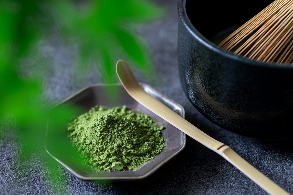 六角皿に盛られた抹茶粉末と手前に置かれた竹の茶杓と黒い茶碗