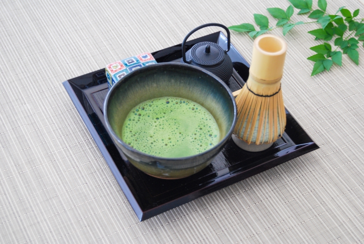 泡立った抹茶が入った茶碗と茶筅と急須が黒い盆に置かれたセット