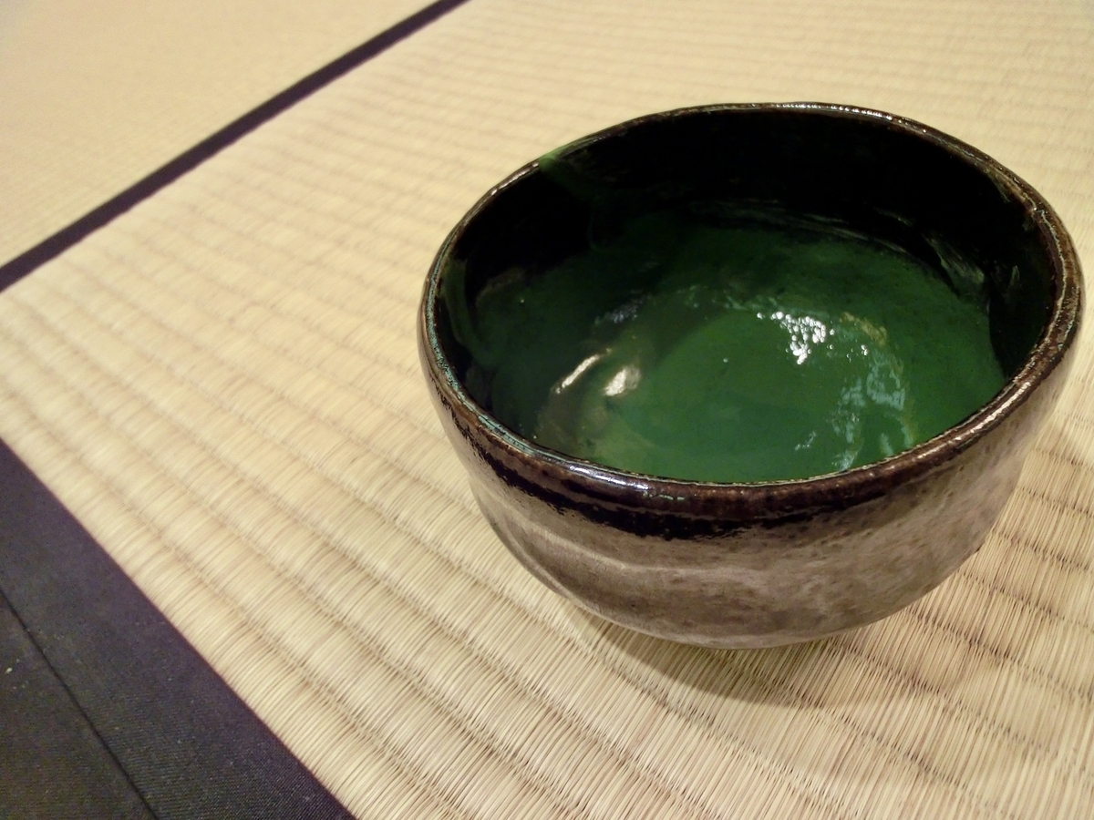 畳の上に置かれた陶器の茶碗に入った艶のある濃茶