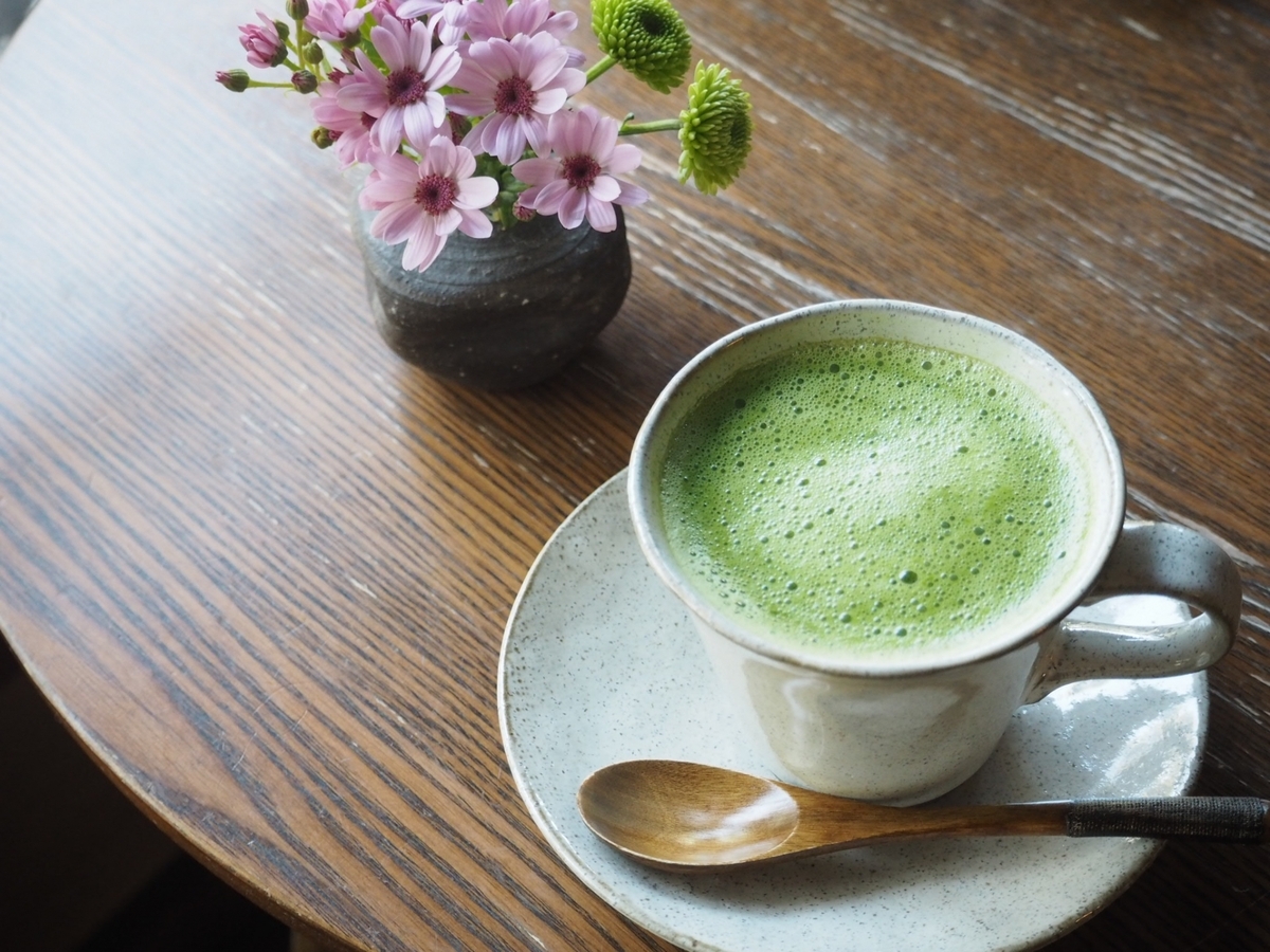 木製テーブルに置かれた抹茶ラテのカップとソーサーと木のスプーン