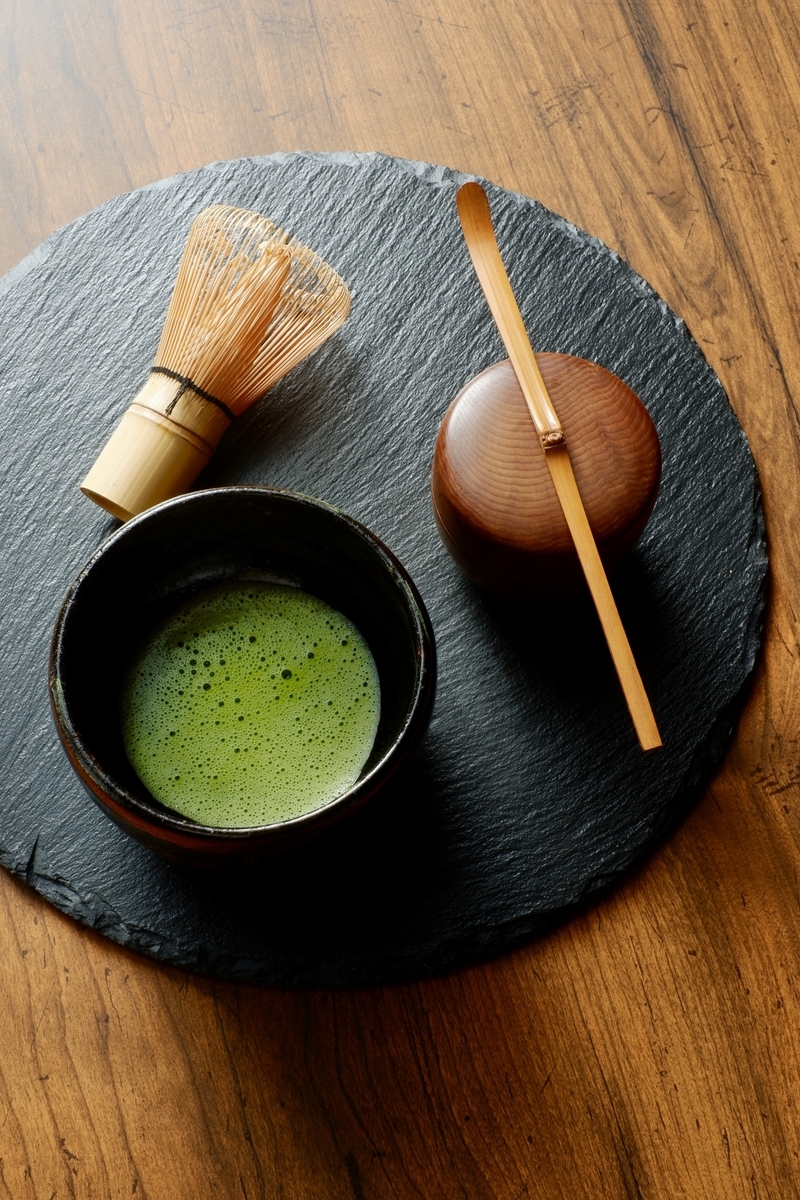 黒い円形の敷板に置かれた抹茶の茶碗と茶筅と棗と茶杓