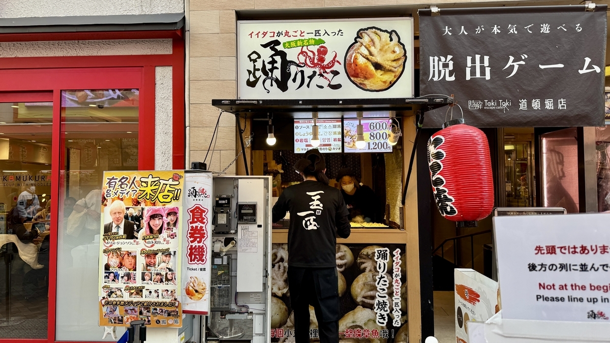 Odoridako Dotonbori storefront with large signs, ticket machine, and staff grilling takoyaki