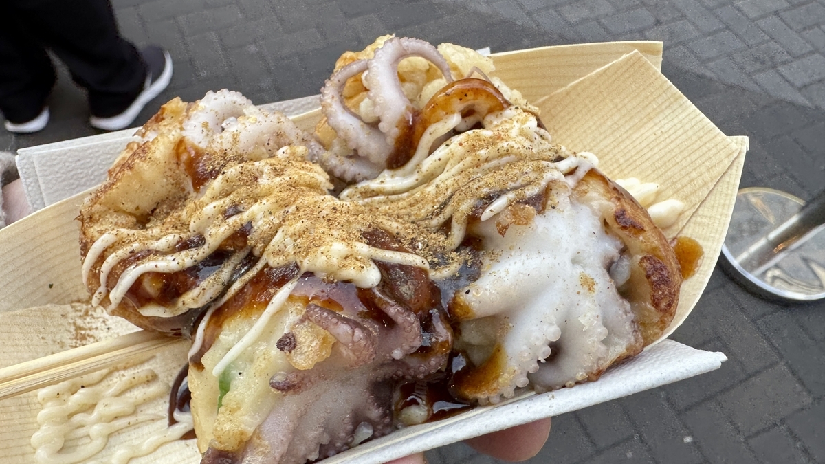 Takoyaki with whole baby octopus topped with sauce and mayonnaise in a takeout container