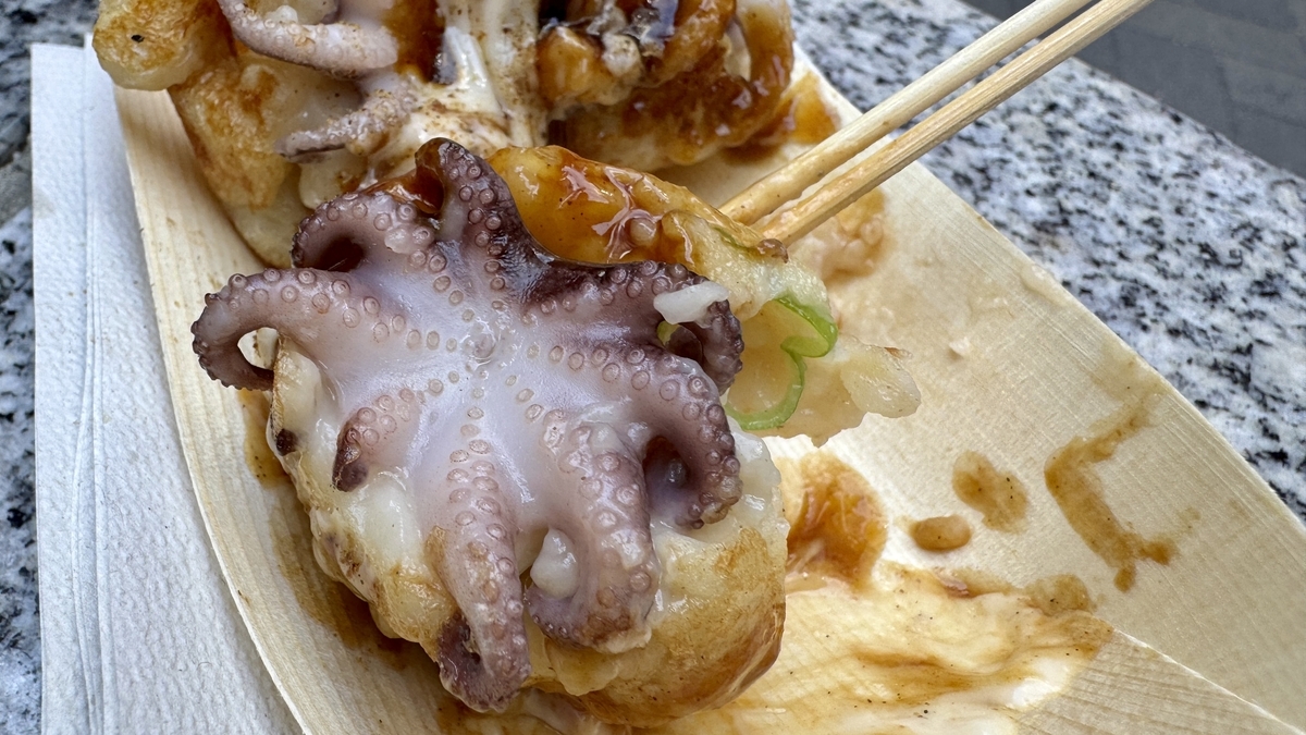 Close-up of chopsticks lifting a takoyaki ball with a whole baby octopus on top