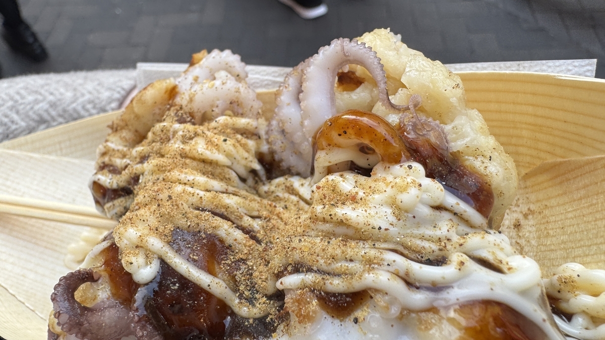 Three takoyaki balls with baby octopus legs sticking out, topped with sauce and mayonnaise on a wooden plate