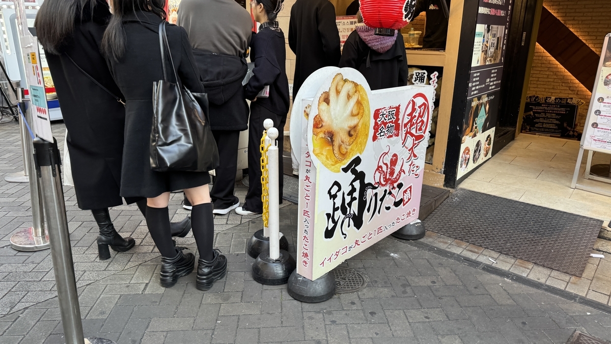 Odoridako storefront sign featuring whole octopus takoyaki with customers lining up