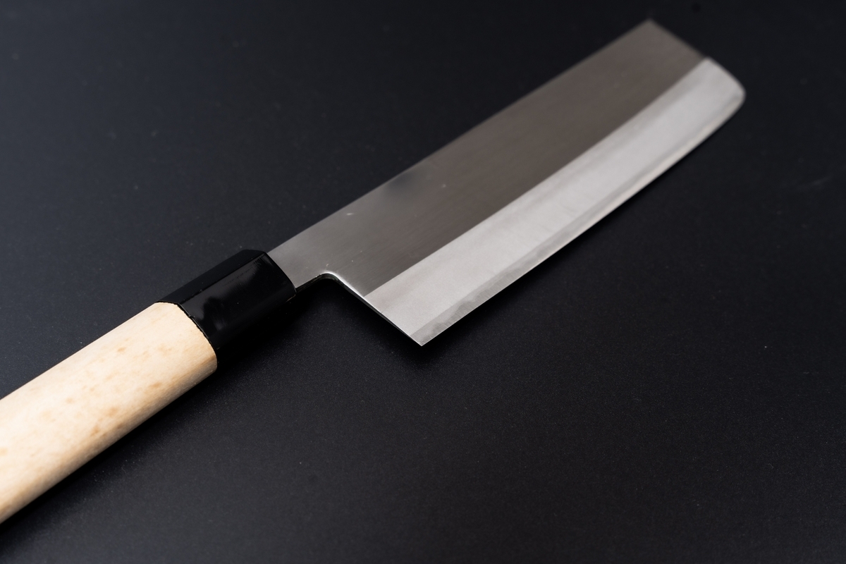 A Nakiri knife with a rectangular blade and white wooden handle against a black background