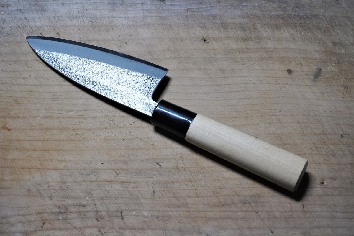 A thick Deba knife with a hammered finish on the blade, placed on a wooden board