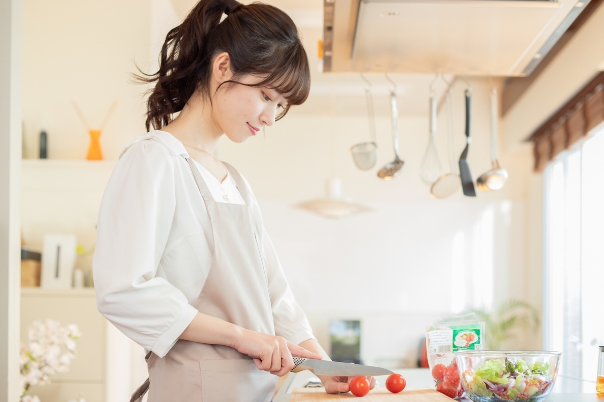 A woman in an apron slicing cherry tomatoes with a knife in a bright kitchen
