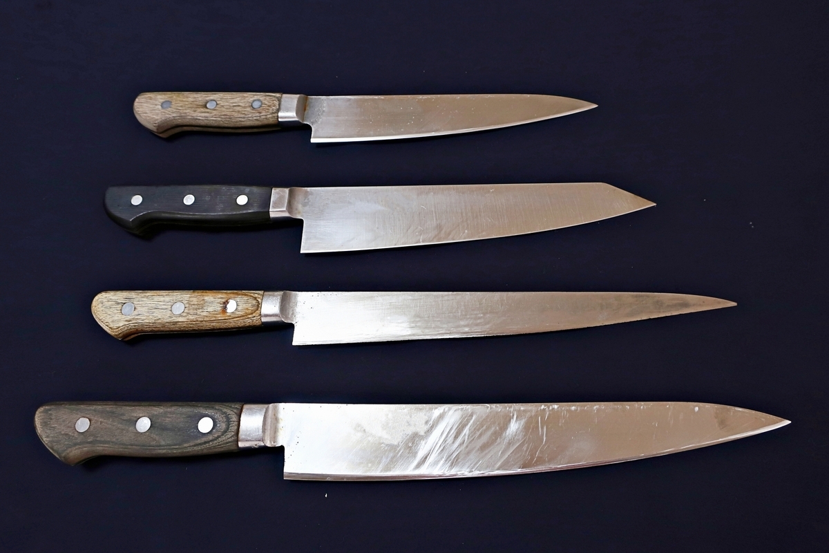Four knives with different handles and blade shapes arranged against a black background