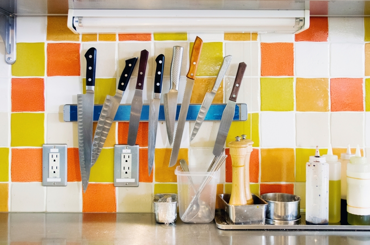 Multiple knives stored on a magnetic holder against a colorful tiled kitchen wall