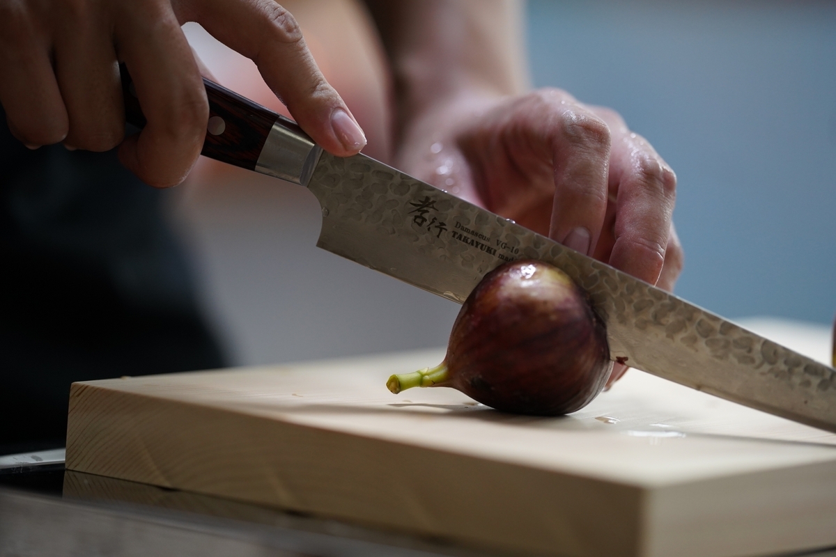 Close-up of hands slicing figs with a Japanese knife on a wooden cutting board