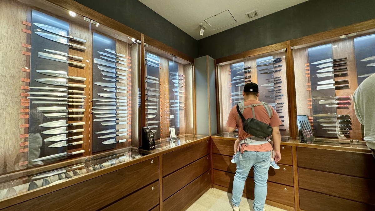 Interior of Tower Knives Tokyo with rows of knives displayed in wooden showcases and customers comparing blades