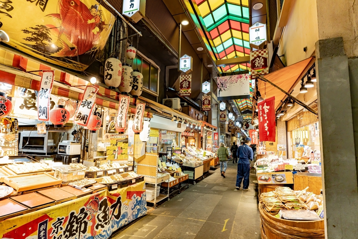 Tourists walking through Nishiki Market arcade with rows of lanterns and food stalls
