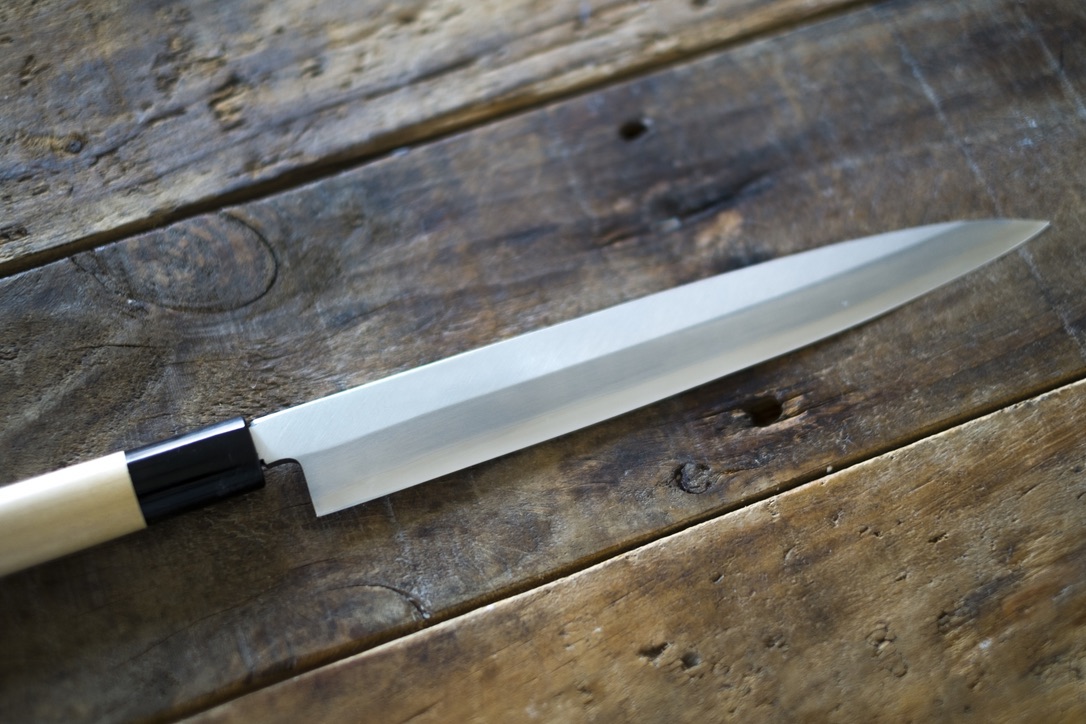 Full view of a yanagiba knife with a natural wood handle on a wooden workbench