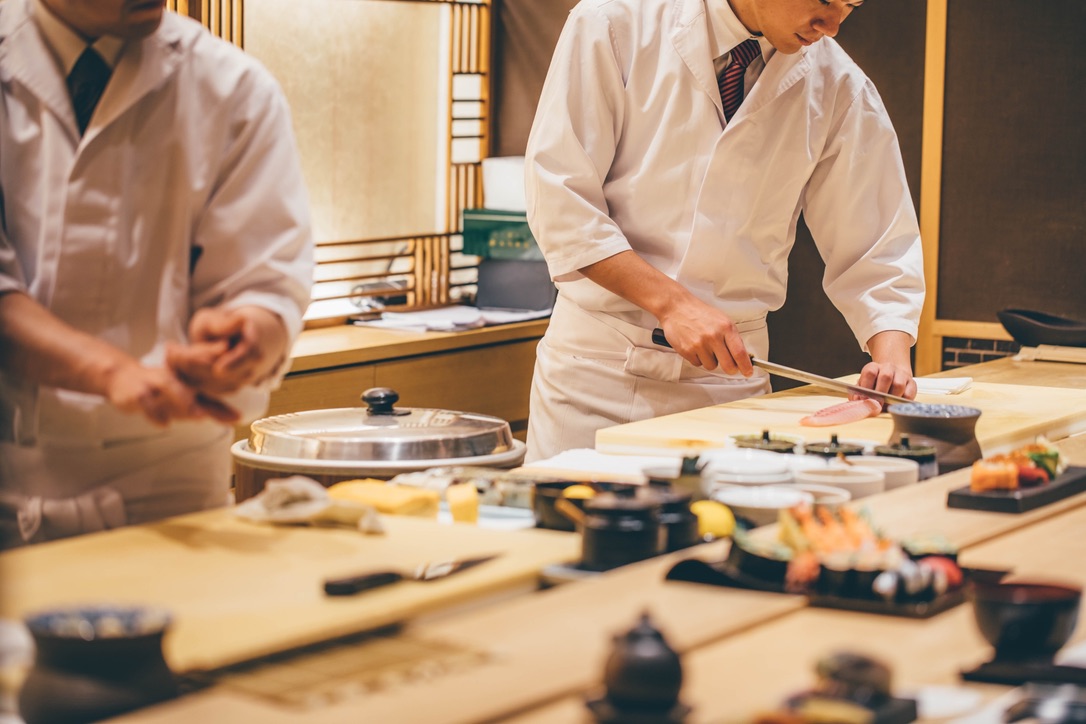 A sushi chef slicing ingredients with a knife at the counter