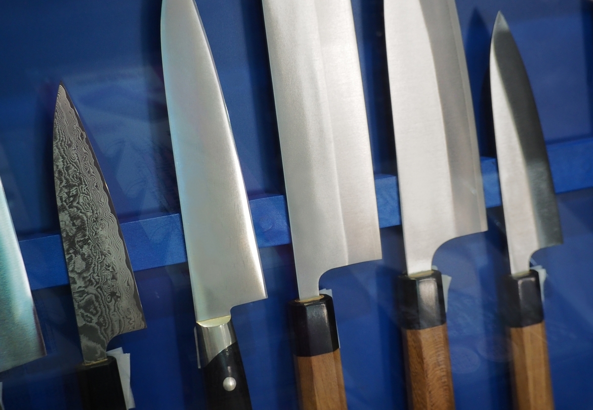 Various knives including gyuto and santoku displayed on blue cloth showing blade edges and wooden handles