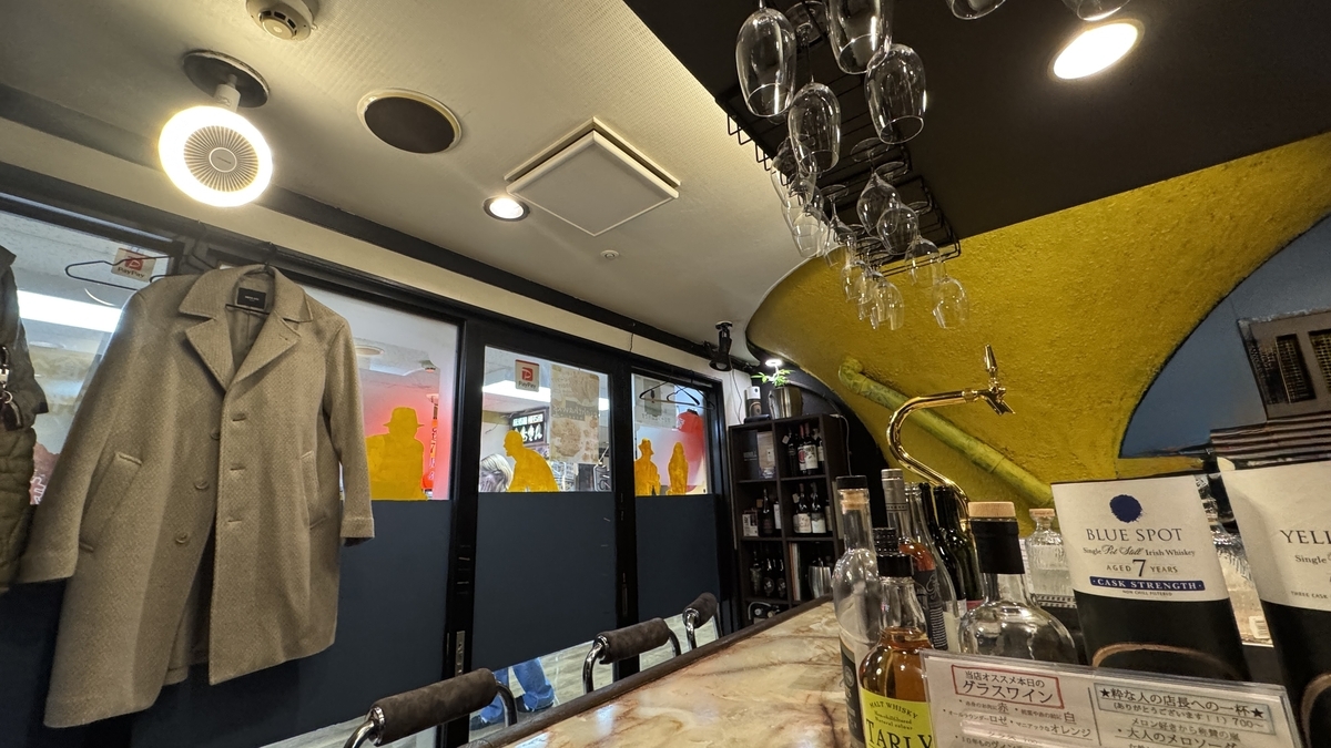 內部空間展示大理石風格吧台，天花板懸掛著酒杯，藍黃雙色牆面擺滿酒瓶和酒龍