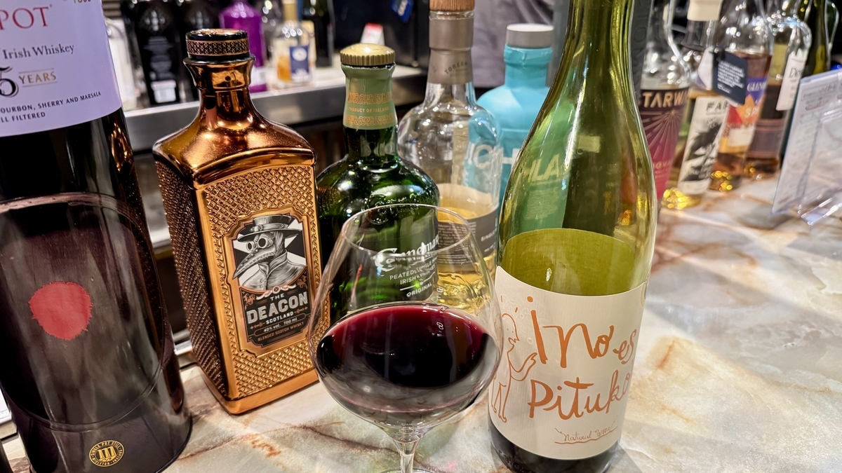 吧台上的一杯紅酒和酒瓶，威士忌和琴酒瓶襯托出酒吧氛圍