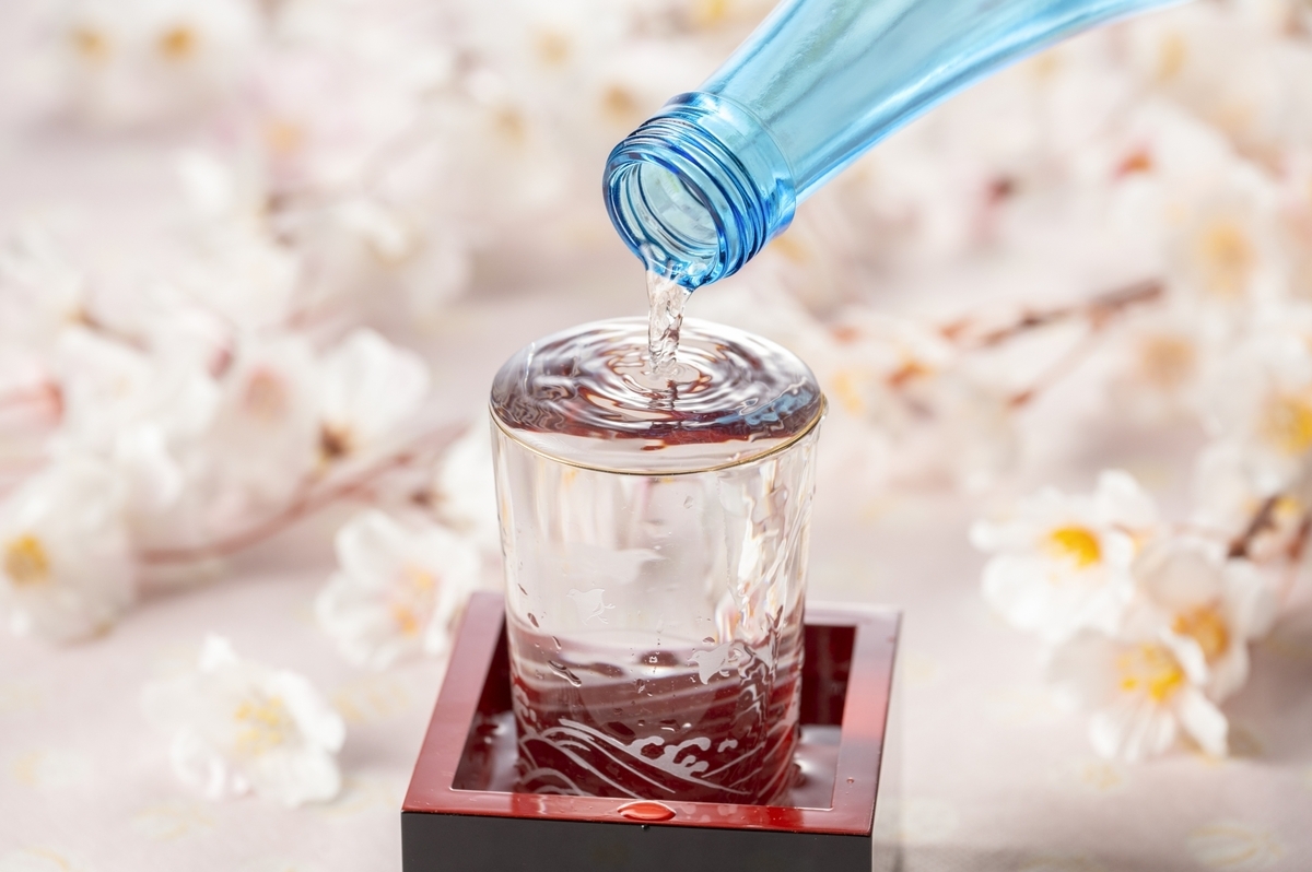 สาเกถูกรินจากขวดลงในแก้วที่วางอยู่บนมาสุ