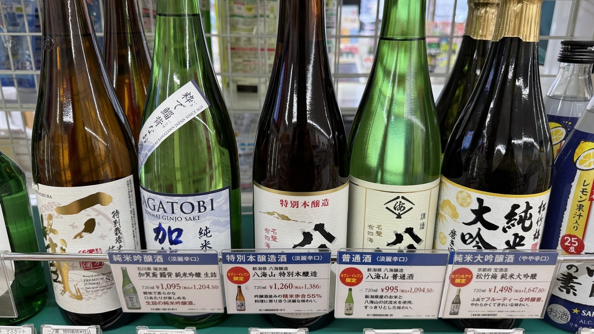 편의점 진열대에 나란히 놓인 여러 브랜드의 사케 병과 가격표 클로즈업