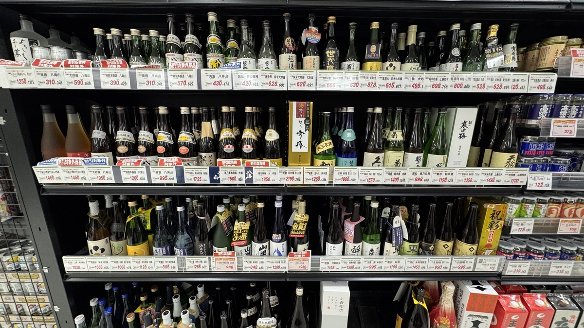 슈퍼마켓의 냉장 진열대 가득 나란히 놓인 사케 병과 가격표가 이어지는 매장