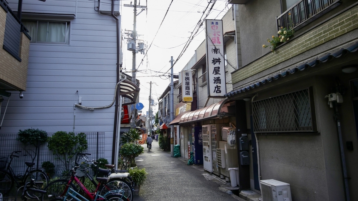 주택가의 좁은 골목에 서 있는 오래된 주류점의 간판과 자전거가 보이는 거리 풍경