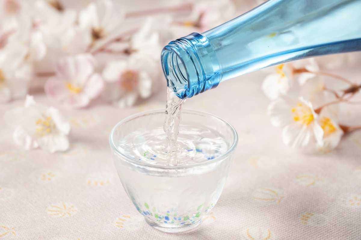 벚꽃을 배경으로 파란 병에서 유리잔으로 사케를 따르는 봄 분위기의 장면