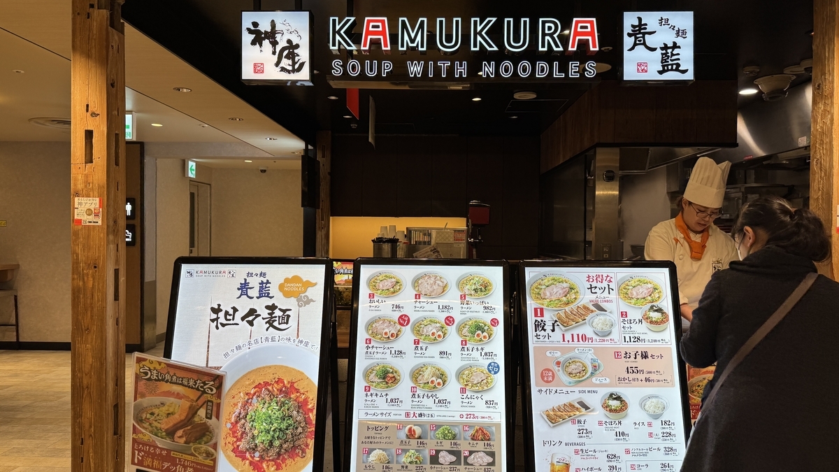 카무쿠라와 세이란의 공동 간판 아래 면 요리 메뉴 보드가 줄지어 있는 주문 카운터