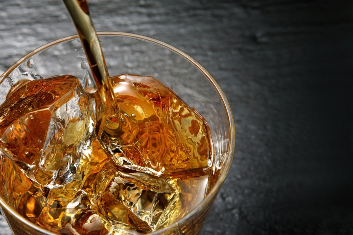 氷を入れたグラスにウイスキーを注ぐ手元を近接で捉えた写真