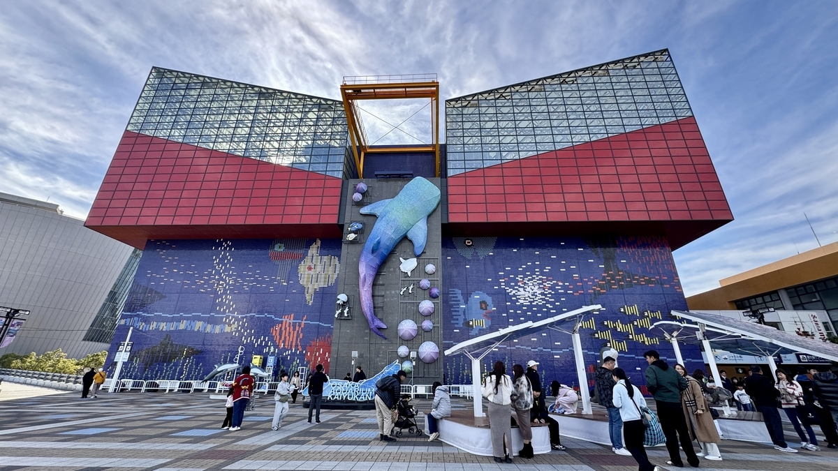 大阪海游馆正面外观,巨大的鲸鲨雕塑和海洋马赛克壁画前游客们正在排队入馆