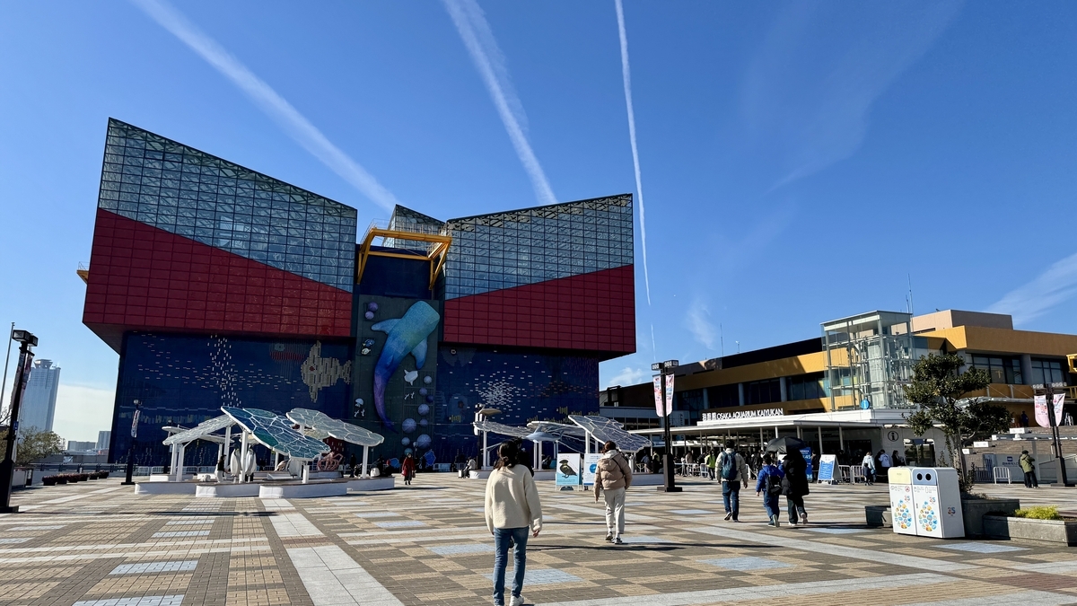 ผู้เยี่ยมชมเดินอยู่บริเวณลานหน้าอาคารพิพิธภัณฑ์สัตว์น้ำโอซาก้า ไคยูคัง ท่ามกลางท้องฟ้าสีคราม