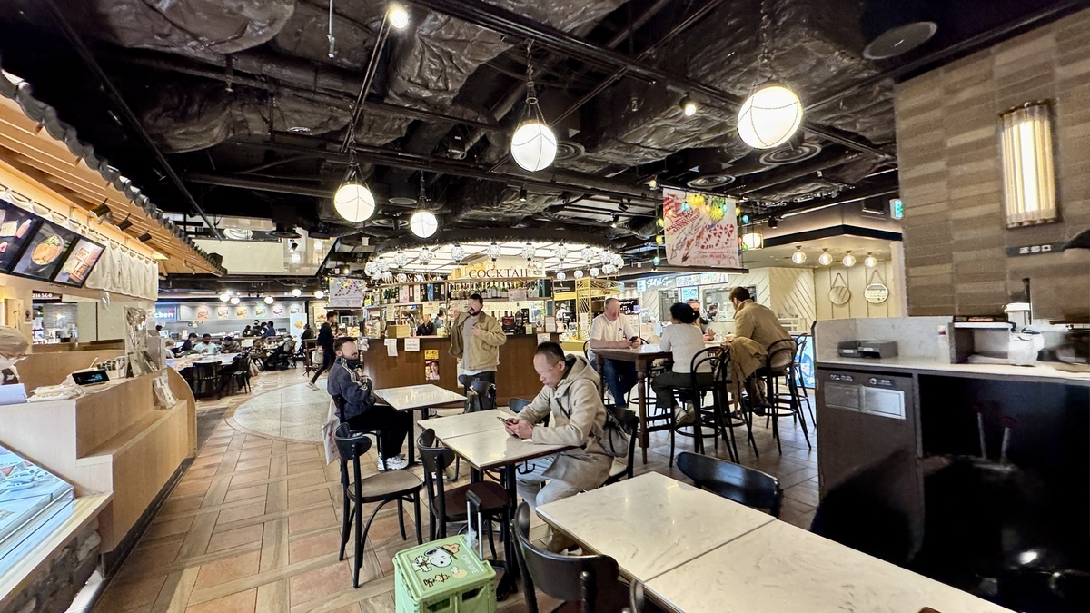 丸い照明が並ぶ共有席エリアで食事を楽しむ来店客