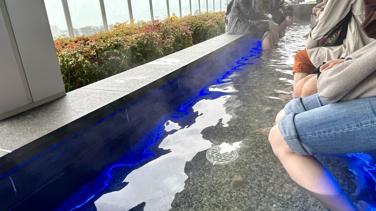 ผู้มาเยือนกำลังเพลิดเพลินกับการแช่เท้าในออนเซ็นธรรมชาติที่ Tenbo Ashiyu Teien