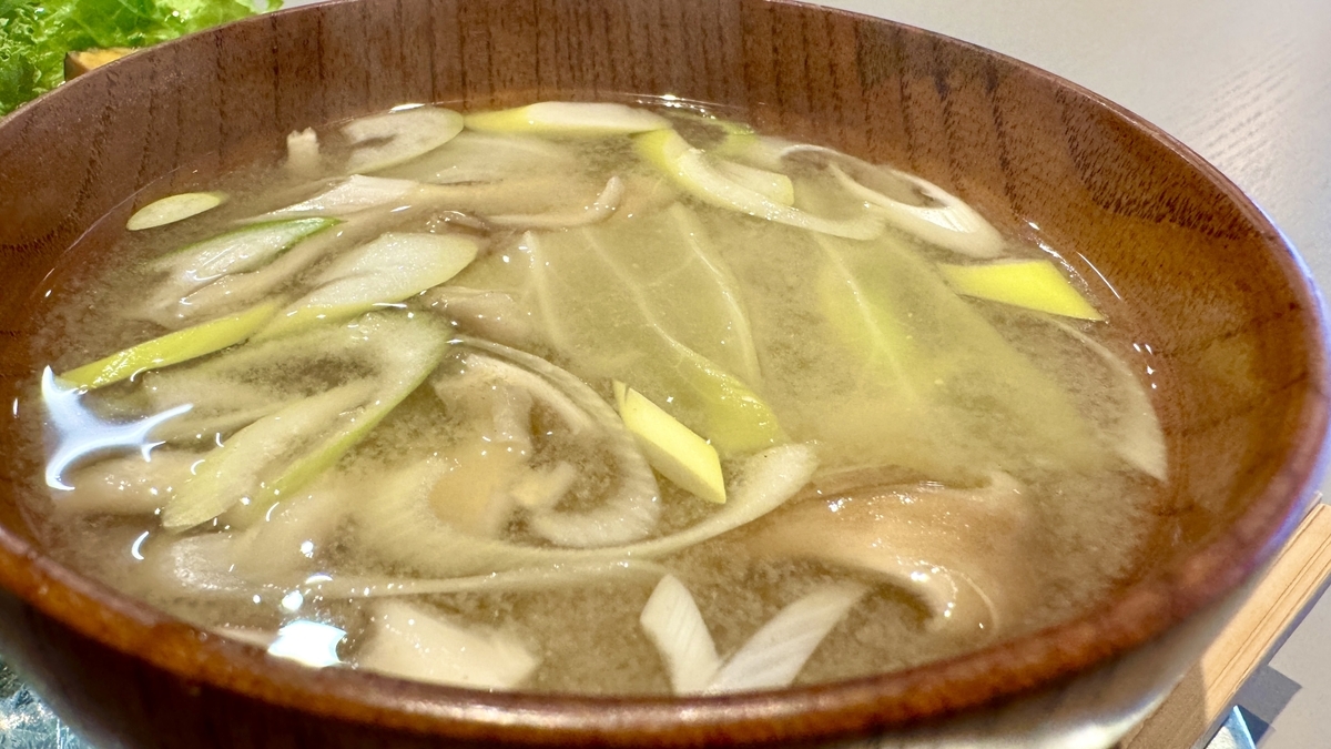 A wooden bowl of miso soup with green onion and mushrooms