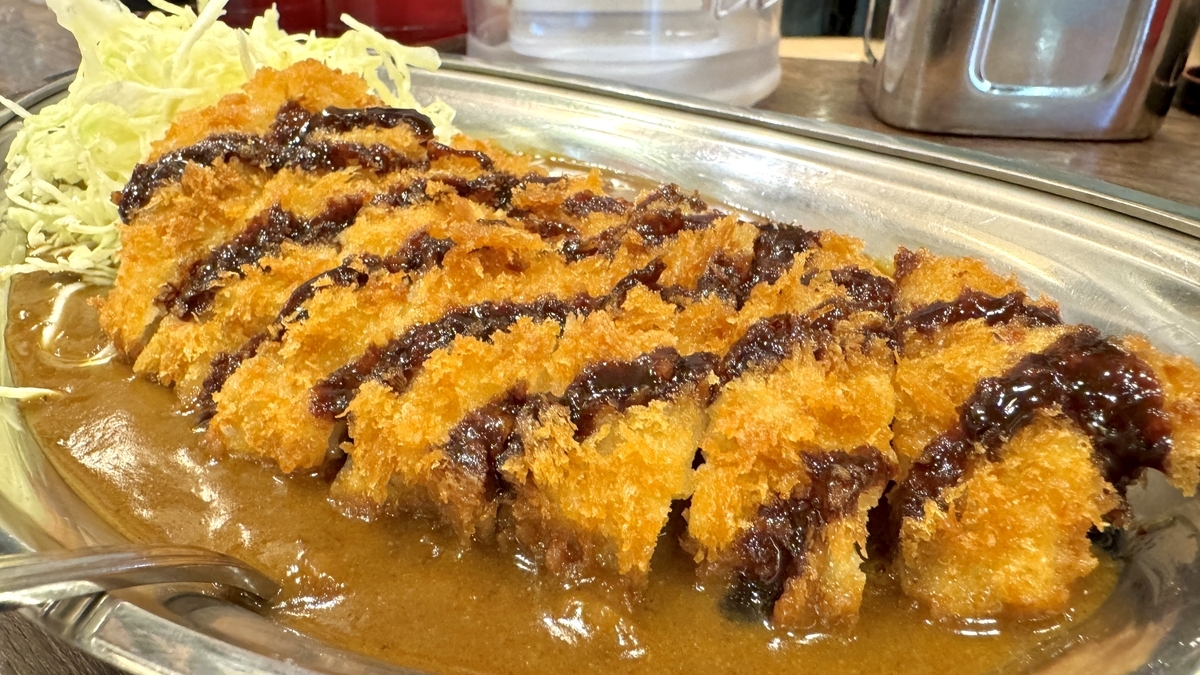 Primer plano de una chuleta L-Katsu con salsa sobre una rica salsa de curry