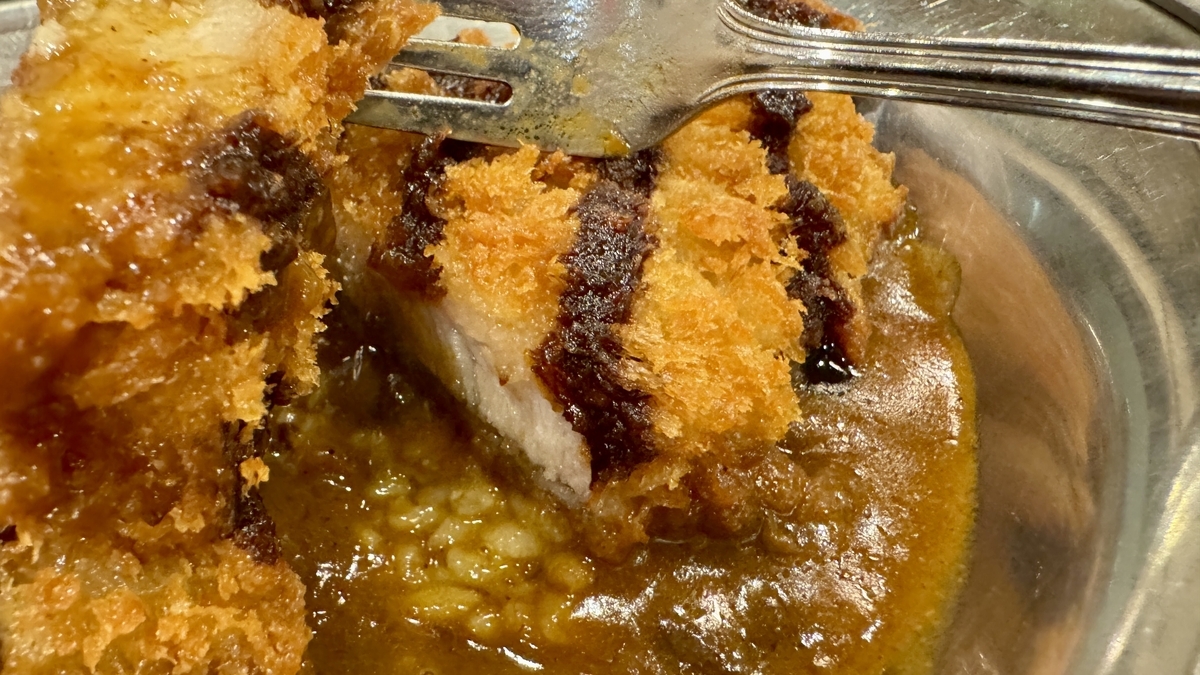 Sección de una chuleta de corte grueso levantada con un tenedor sobre la salsa de curry