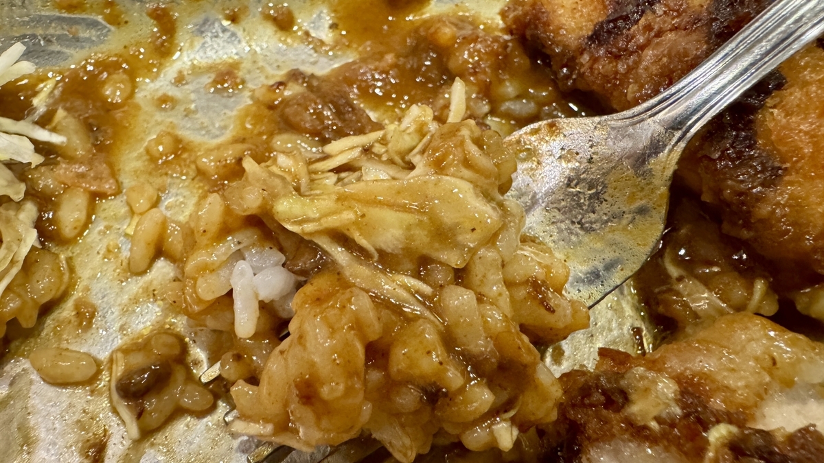 Tenedor cargado con arroz cubierto de salsa de curry junto con col en juliana