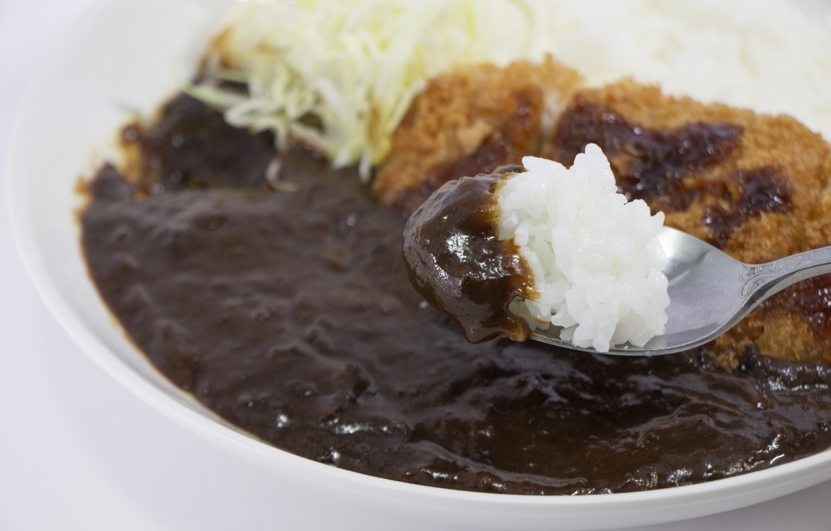 Cuchara recogiendo roux negro denso y cutlet de un plato de Curry de Kanazawa