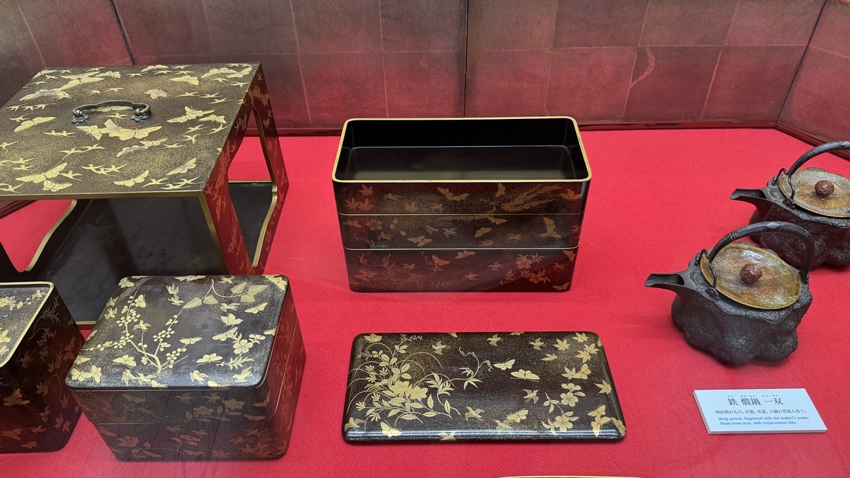 金莳绘层叠食盒、文箱与铁壶并排陈列的展品