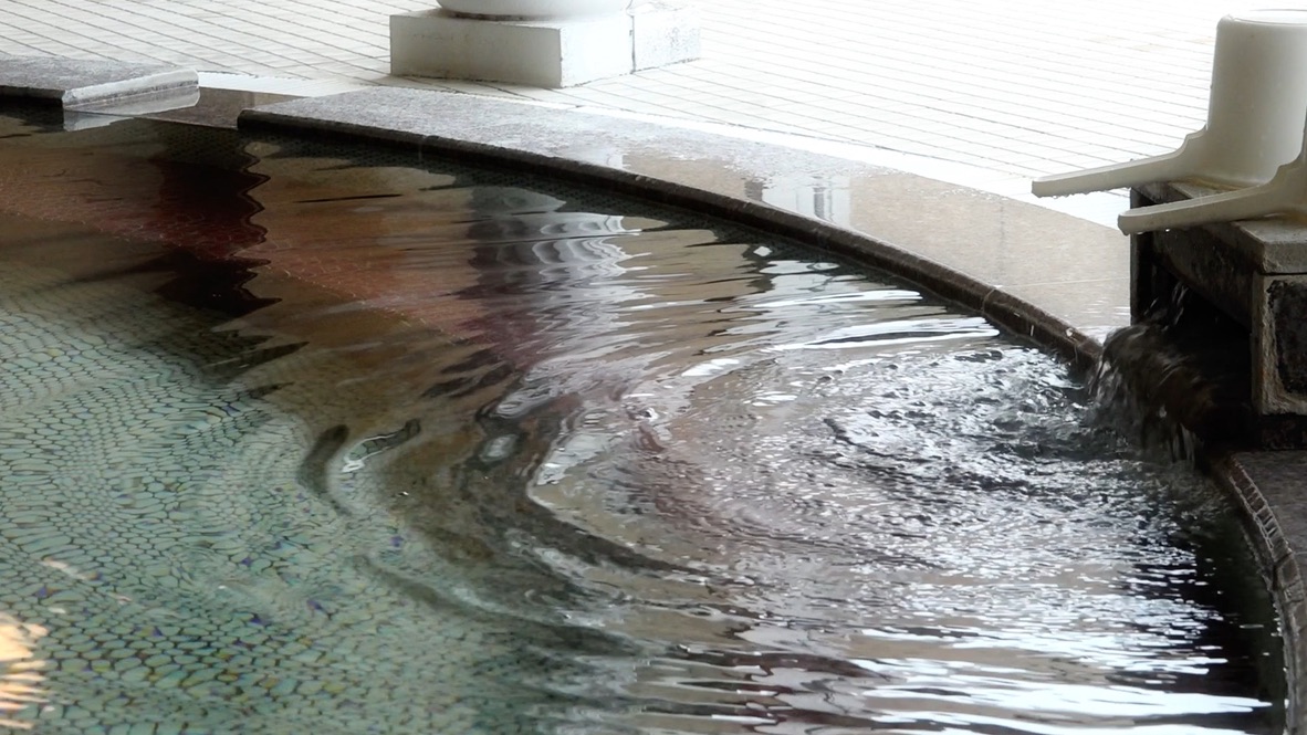 Clear hot spring water flowing into an indoor bathtub from the spout