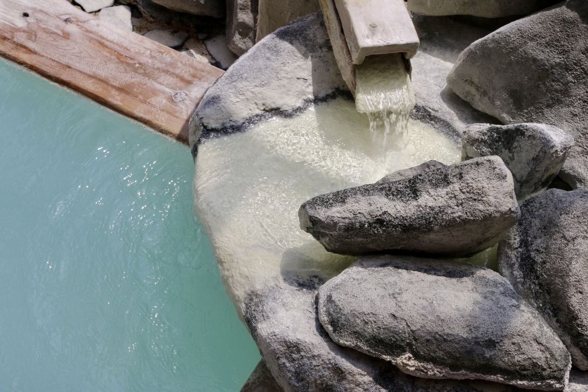 Milky white sulfur spring water pouring from the spout into a stone bath