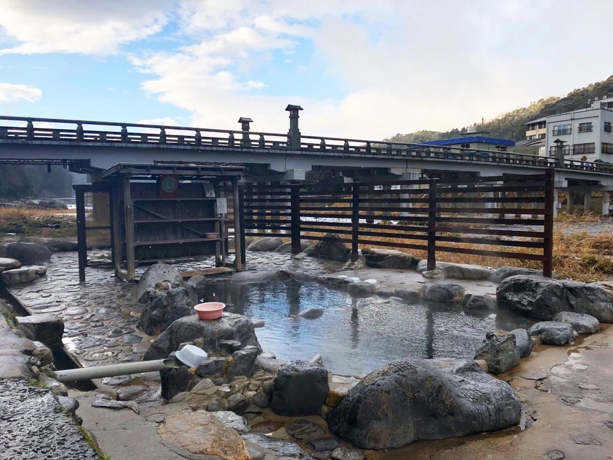 Stone open-air bath beside a river, with steam rising from the water