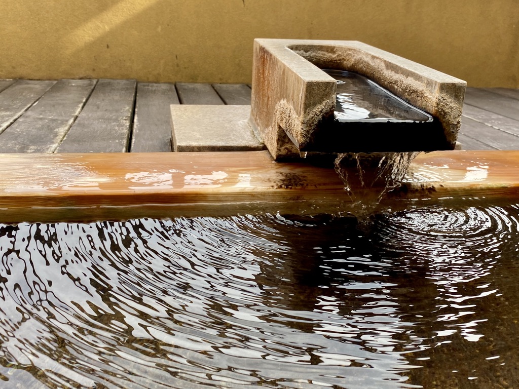 Brown hot spring water flowing from a wooden spout into a bathtub