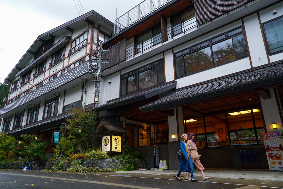 La fachada del ryokan Chitose en Matsunoyama Onsen y gente paseando por el pueblo termal