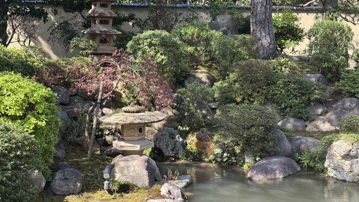 池のほとりに灯籠と築山の植栽が配された千田家庭園