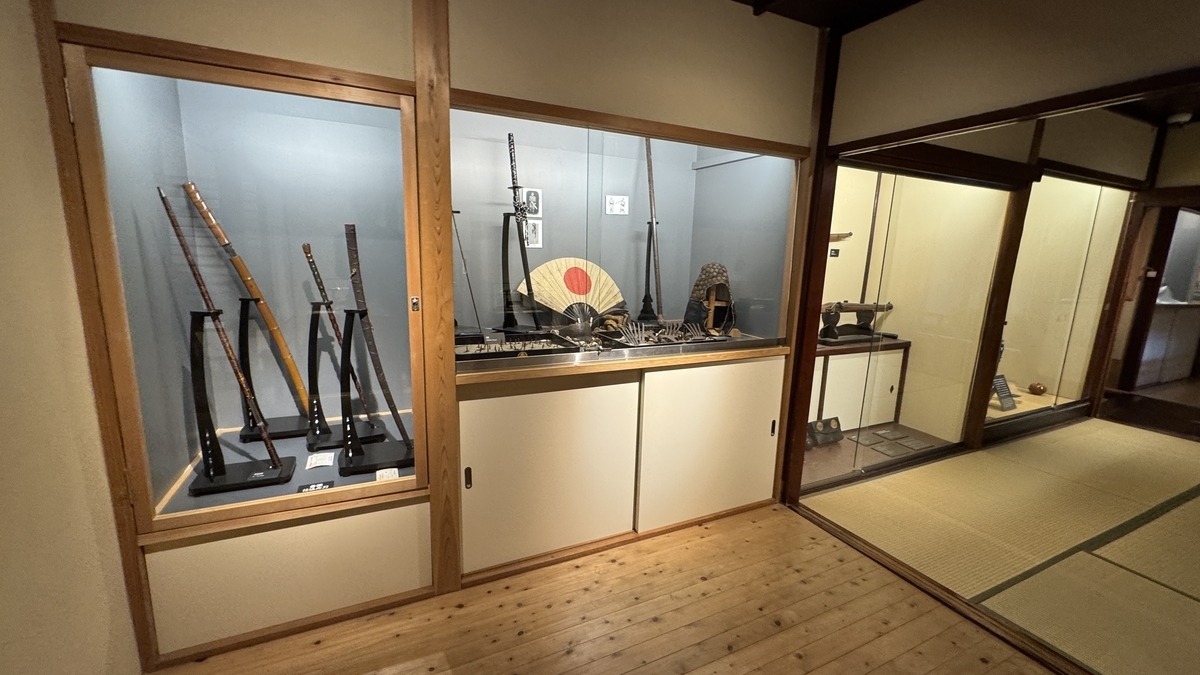 A tatami-floored exhibition room lined with swords and matchlock guns