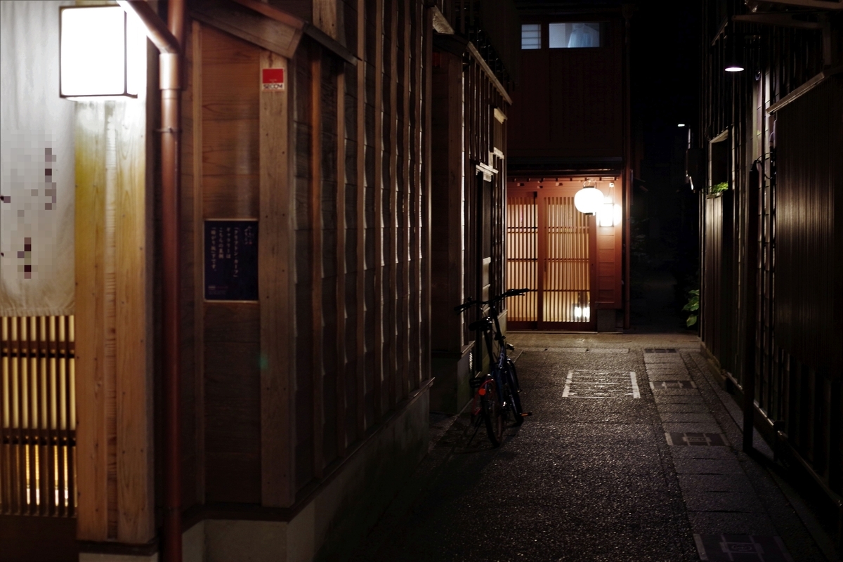 A narrow alley in Kazuemachi Chaya District at night, with light glowing through the lattice doors