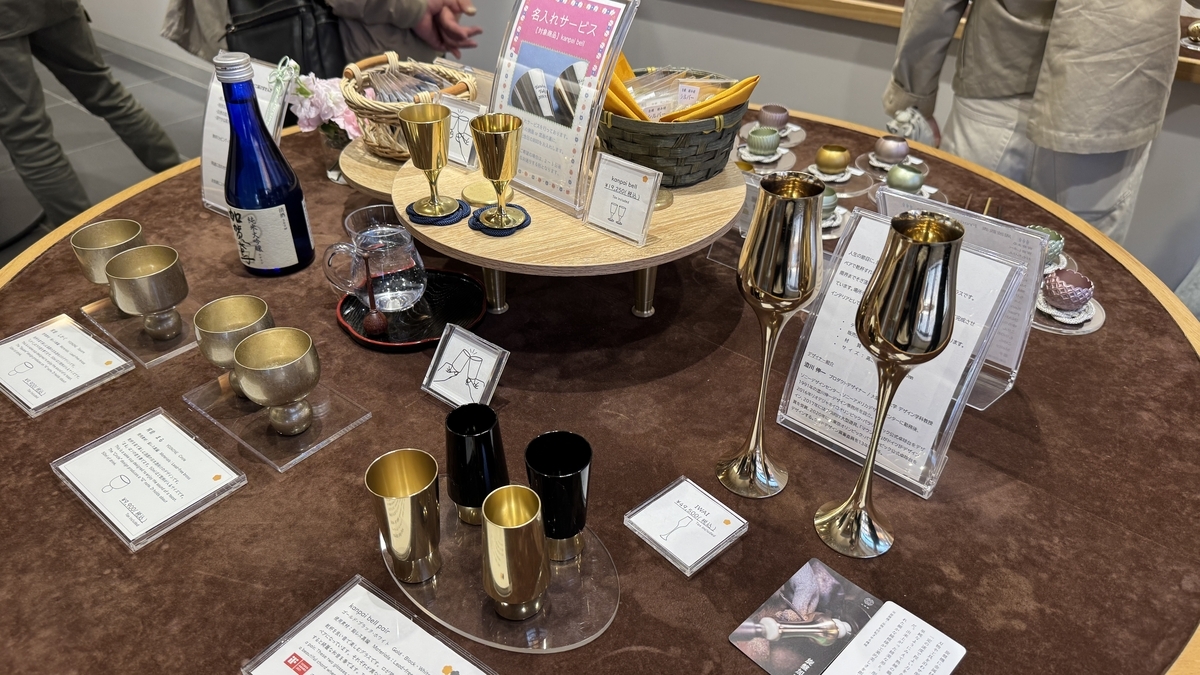 Recipientes de sake dorados y copas expuestos en Koizumiya Kanazawa